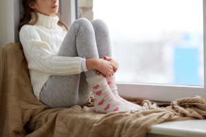 Jeune femme pelotonnée devant la fenêtre en tenue douillette